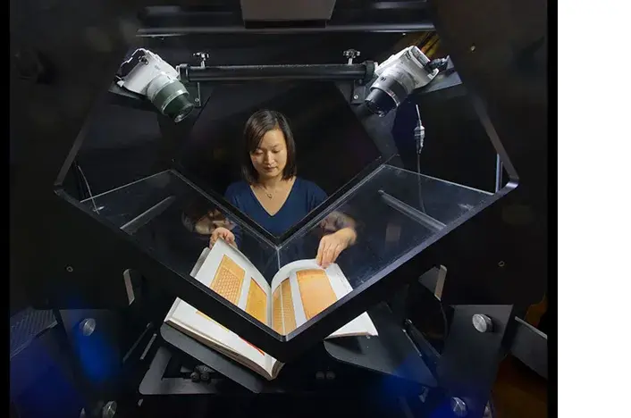 Une opératrice utilise un scanner en V de type Table Top Scribe sur un livre relié
