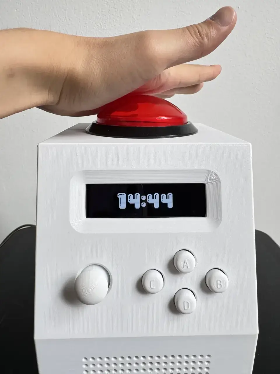 Une main frappe le grand bouton arcade de 100 mm placé sur le dessus de CinderClock