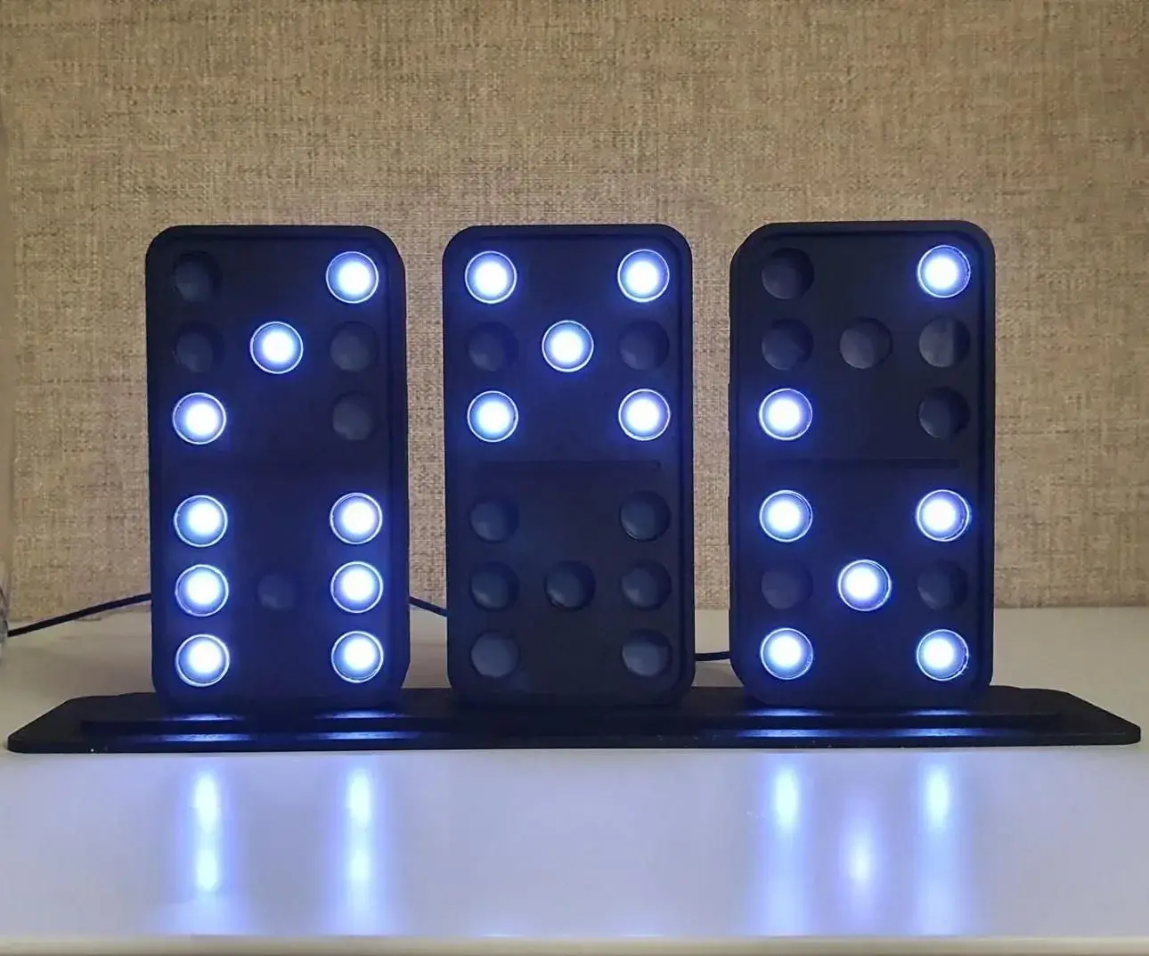 Trois dominos noirs posés sur une base affichent 9 h 53 en points bleus lumineux