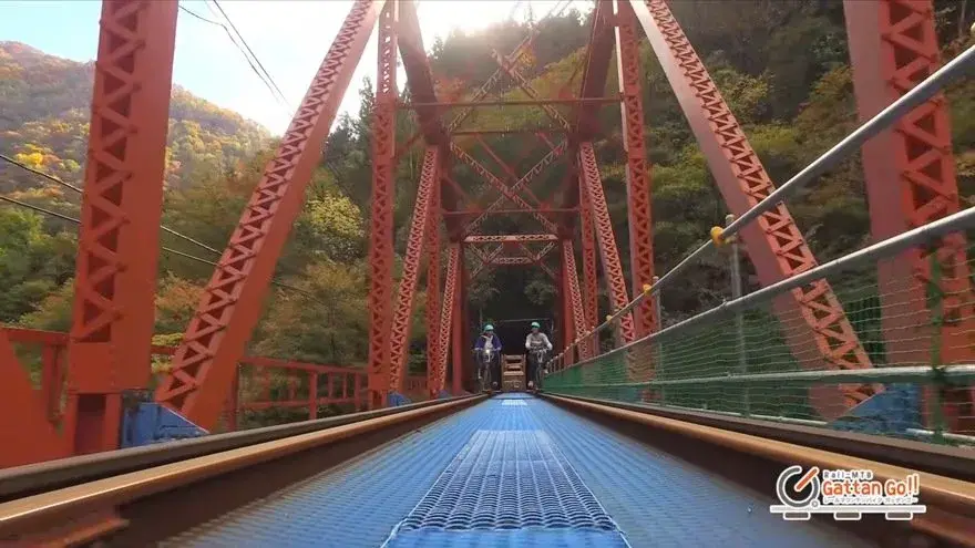 Deux cyclistes franchissent le pont rouge de la deuxième rivière Takahara sur un vélo-rail électrique, dans les gorges d'Urushiyama