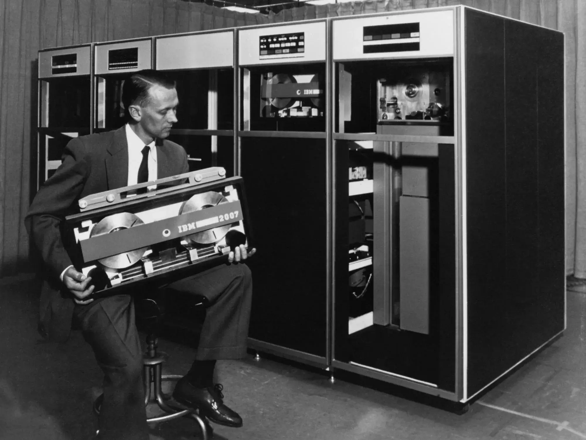 Un technicien IBM tient une cassette de bande Tractor devant des meubles de lecteurs